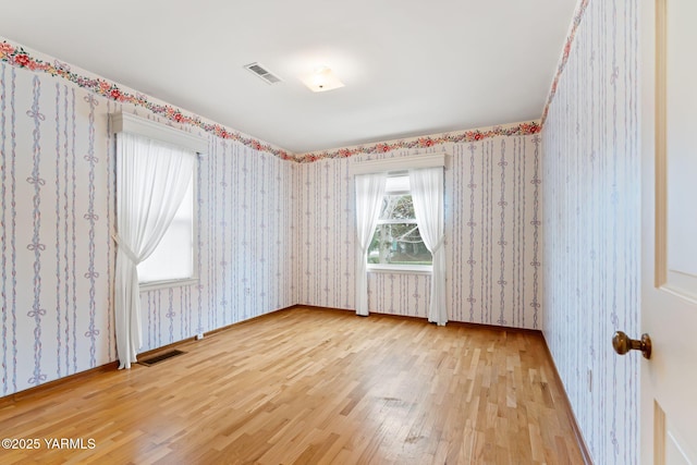 spare room featuring wood finished floors, visible vents, baseboards, and wallpapered walls