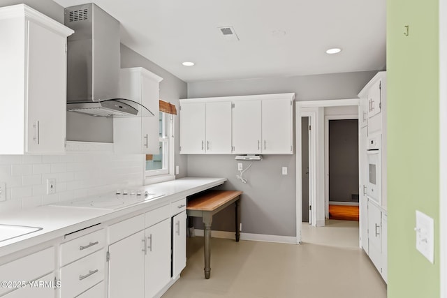 kitchen with white appliances, light countertops, wall chimney range hood, and white cabinetry