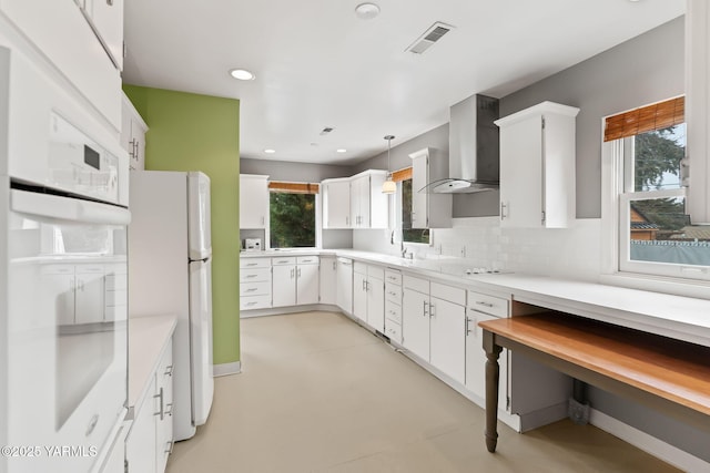 kitchen with white cabinets, light countertops, wall chimney range hood, freestanding refrigerator, and decorative light fixtures