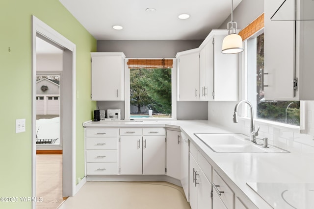 kitchen with decorative backsplash, hanging light fixtures, light countertops, white cabinetry, and a sink