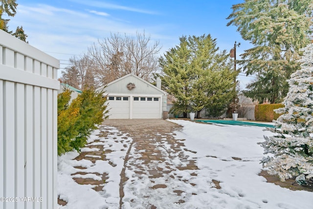 yard covered in snow with a garage, an outbuilding, and fence