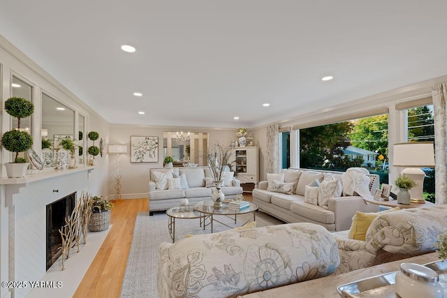 living room featuring light wood-style flooring, recessed lighting, a fireplace with flush hearth, ornamental molding, and an inviting chandelier