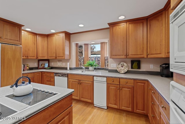 kitchen featuring white appliances, a sink, light countertops, light wood-type flooring, and brown cabinetry