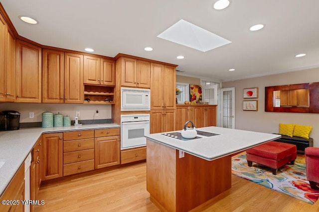 kitchen with a kitchen island with sink, white appliances, a skylight, light wood-style floors, and light countertops