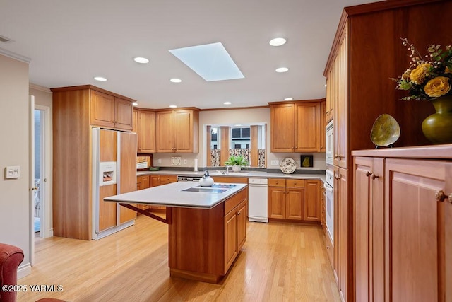 kitchen with a skylight, a kitchen island, paneled refrigerator, light countertops, and light wood-style floors