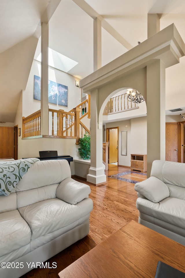 living area with baseboards, stairway, decorative columns, wood finished floors, and high vaulted ceiling