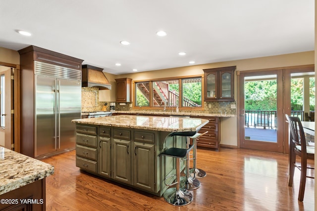 kitchen with premium range hood, built in refrigerator, backsplash, and a healthy amount of sunlight