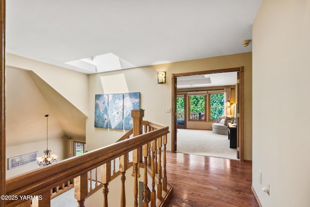 corridor featuring wood finished floors, an upstairs landing, a notable chandelier, and a skylight