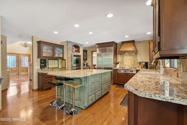 kitchen featuring premium range hood, a sink, light wood-style floors, a breakfast bar area, and decorative backsplash