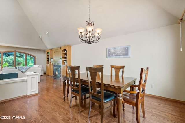 dining room with baseboards, a fireplace with flush hearth, light wood-type flooring, an inviting chandelier, and high vaulted ceiling