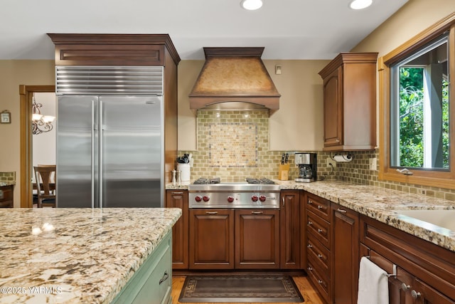 kitchen with custom exhaust hood, appliances with stainless steel finishes, tasteful backsplash, and light stone countertops