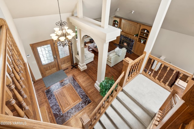 entryway featuring a notable chandelier, a glass covered fireplace, high vaulted ceiling, and wood finished floors