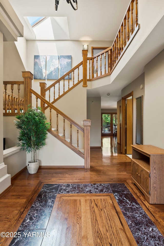 foyer with wood finished floors, stairway, a skylight, baseboards, and a towering ceiling