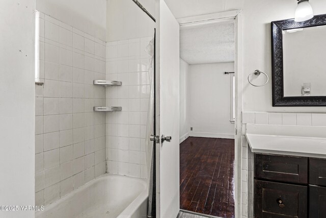 full bath with shower / bathtub combination, a textured ceiling, vanity, wood finished floors, and baseboards