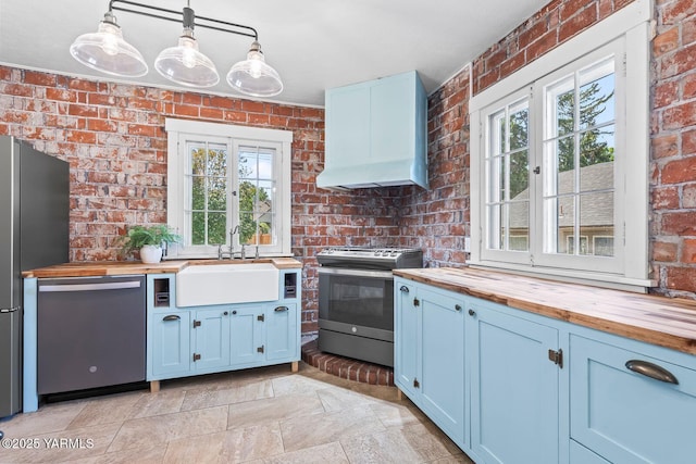 kitchen featuring wooden counters, a sink, stainless steel appliances, brick wall, and stone tile flooring