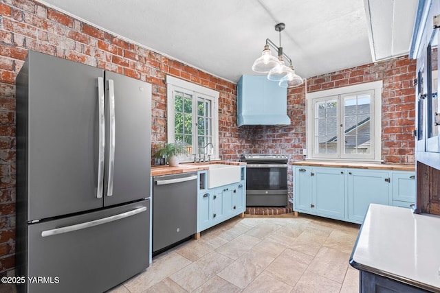 kitchen featuring butcher block countertops, a sink, custom exhaust hood, brick wall, and appliances with stainless steel finishes