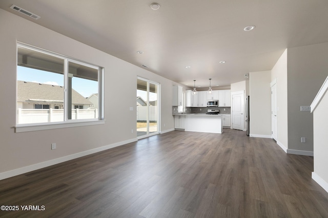 unfurnished living room with baseboards, visible vents, and dark wood-style flooring