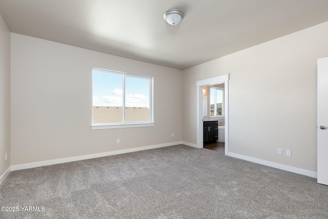 unfurnished bedroom featuring baseboards, dark colored carpet, and ensuite bathroom