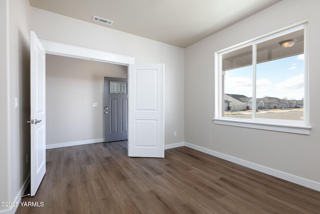 unfurnished room featuring dark wood-type flooring, visible vents, and baseboards