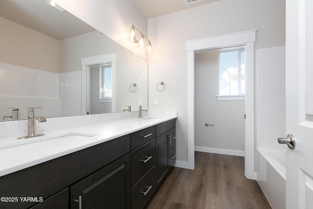 full bathroom with double vanity, wood finished floors, a sink, and baseboards