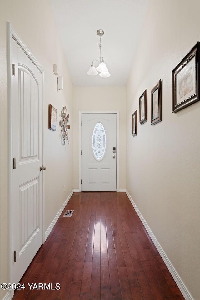 doorway to outside with a chandelier, dark wood-style flooring, and baseboards