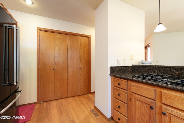 kitchen featuring black gas stovetop, light wood finished floors, brown cabinetry, high end refrigerator, and visible vents