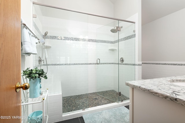 bathroom featuring wainscoting, tile walls, a shower stall, and vanity