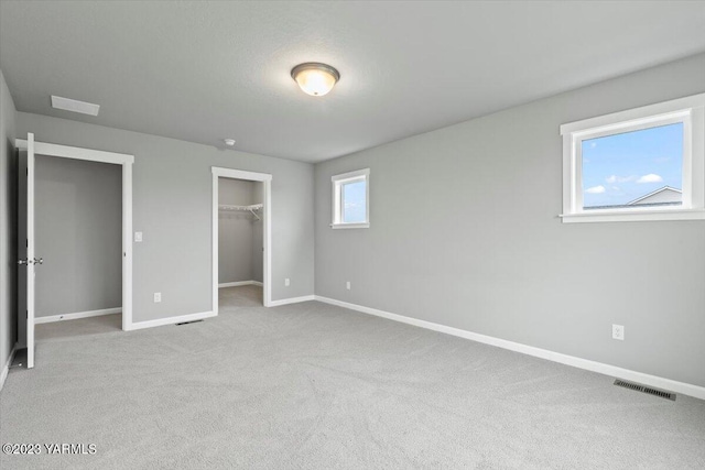 unfurnished bedroom featuring light carpet, visible vents, baseboards, a spacious closet, and a closet