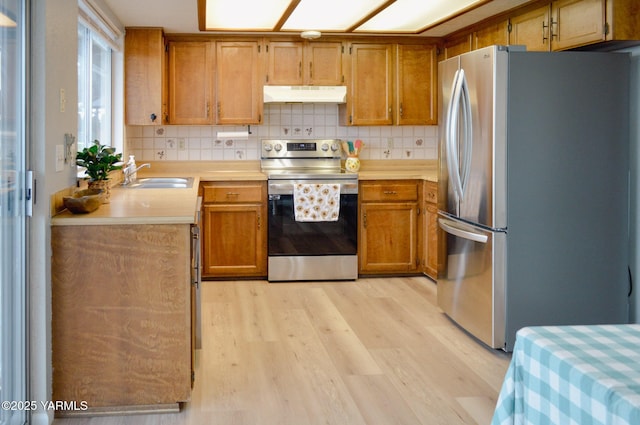 kitchen featuring light countertops, tasteful backsplash, stainless steel appliances, under cabinet range hood, and a sink