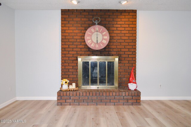 interior details featuring a brick fireplace, a textured ceiling, baseboards, and wood finished floors