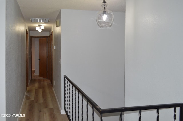hallway with baseboards, visible vents, and wood finished floors
