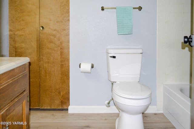 full bath featuring toilet, wood finished floors, vanity, and a tub to relax in