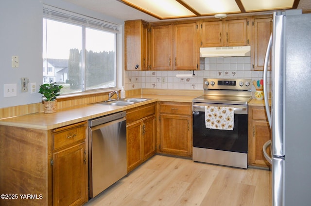 kitchen with light countertops, a sink, appliances with stainless steel finishes, light wood-type flooring, and under cabinet range hood
