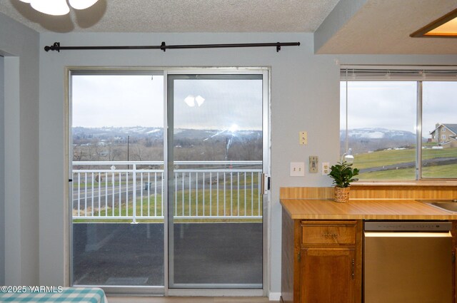 kitchen featuring brown cabinetry, a textured ceiling, stainless steel dishwasher, and light countertops