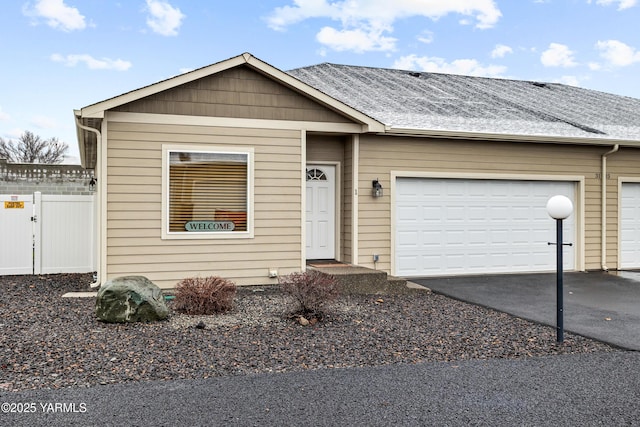 view of front of property with driveway, an attached garage, fence, and roof with shingles