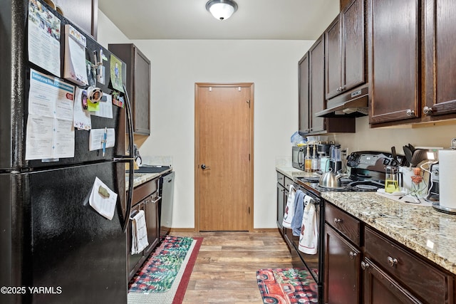 kitchen featuring light stone counters, dark brown cabinetry, light wood-style flooring, under cabinet range hood, and black appliances