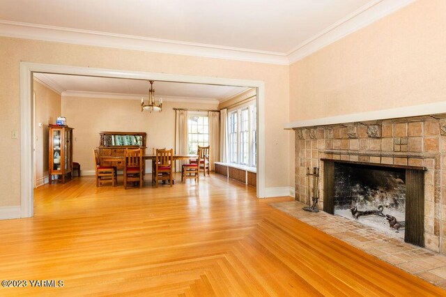 living room featuring ornamental molding, a chandelier, a tiled fireplace, and baseboards