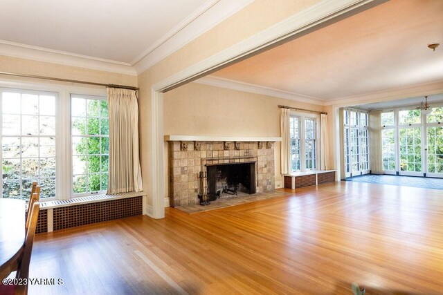 unfurnished living room featuring radiator, a fireplace with flush hearth, crown molding, and wood finished floors