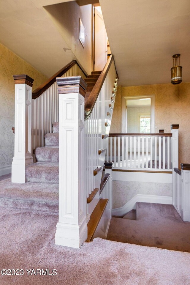 staircase featuring lofted ceiling, wallpapered walls, carpet, and baseboards