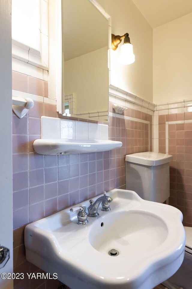 half bathroom with wainscoting, a sink, and tile walls