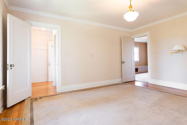 spare room featuring wood finished floors, visible vents, baseboards, ornamental molding, and carpet