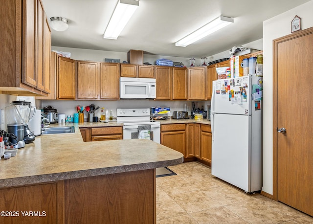 kitchen featuring white appliances, a peninsula, brown cabinetry, and a sink