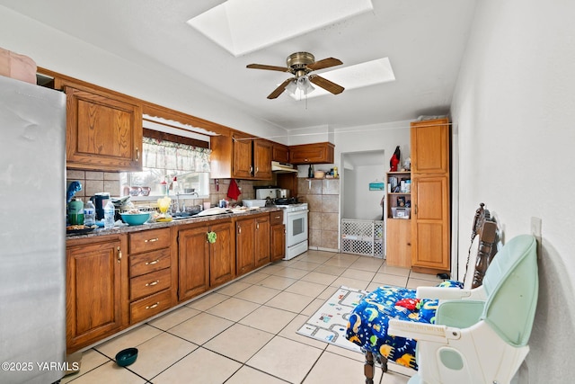 kitchen featuring freestanding refrigerator, a skylight, brown cabinets, and white gas range