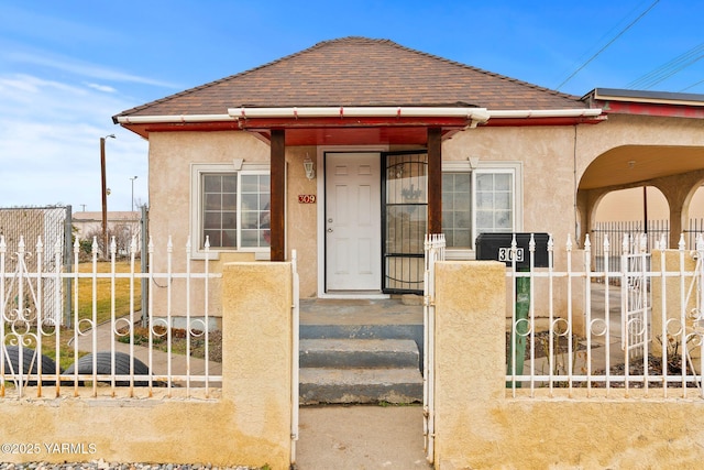 view of front facade featuring a fenced front yard, roof with shingles, and stucco siding