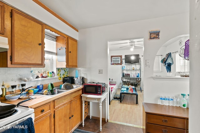 kitchen featuring brown cabinetry, decorative backsplash, ceiling fan, light countertops, and a sink