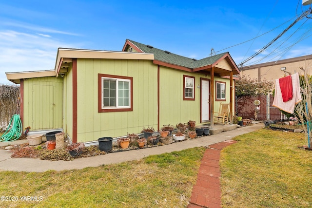 exterior space featuring a shingled roof, fence, and a lawn