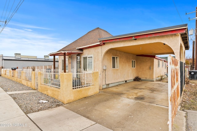 view of side of property featuring an attached carport, a fenced front yard, driveway, roof with shingles, and stucco siding