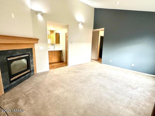 unfurnished living room featuring high vaulted ceiling, a glass covered fireplace, and carpet flooring