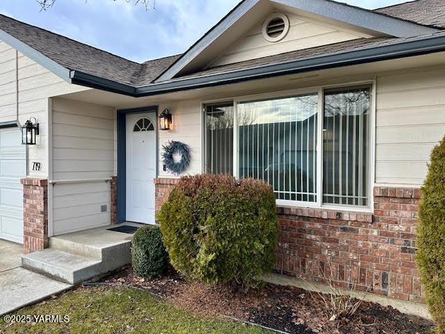 doorway to property featuring an attached garage and brick siding