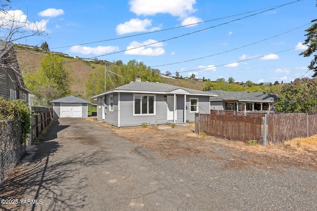 view of front of home featuring an outbuilding, a detached garage, driveway, a chimney, and fence